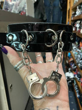 Load image into Gallery viewer, Black leather collar with silver D ring details, and two silver handcuffs hanging from two silver chains.