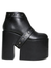 Load image into Gallery viewer, side view of black vegan leather super tall 6" heel, 4" platform sleep design boot. Boot has a rivet studded strap that wraps around and is removable or attachable with Velcro. Boot has black EVA platform.