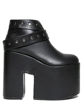 Load image into Gallery viewer, outer side view of black vegan leather super tall 6" heel, 4" platform sleep design boot. Boot has a rivet studded strap that wraps around and is removable or attachable with Velcro. Boot has black EVA platform.