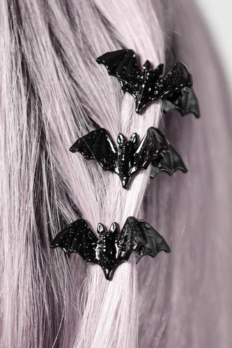Black bat-shaped hair clips on a person's hair against a neutral background