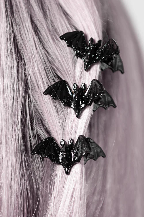 Black bat-shaped hair clips on a person's hair against a neutral background