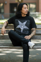 Load image into Gallery viewer, Man sitting on a bench wearing a black t-shirt with a star design, outdoors.
