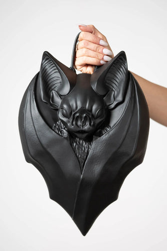 Black bat-shaped handbag held by a person against a white background