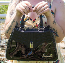 Load image into Gallery viewer, model holding glossy black purse with silver lock detail on front center. The shell is comprised of glossy black faux leather, with matte leather stitched spiderweb details near the top. Zip closure, inner pockets and little metal feet.
