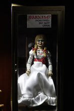 Load image into Gallery viewer, annabelle figure sitting in chair wearing white dress with hair in pig tails. sign reading &quot;warning! positively do not open&quot;
